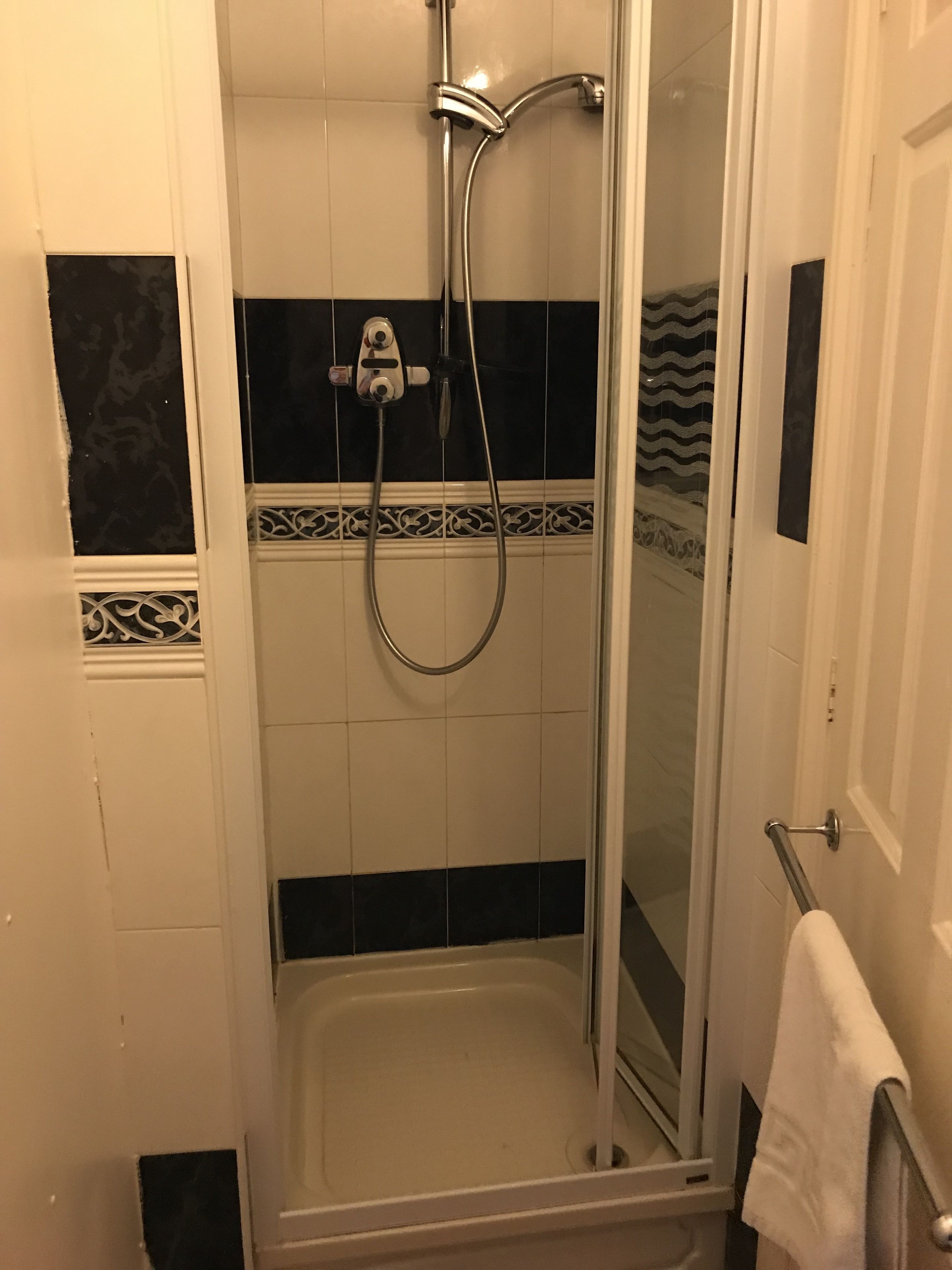 A shower with a glass door, a handheld showerhead, and a handheld faucet.