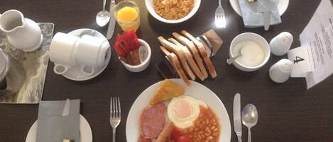 Una mesa de desayuno con platos de huevos, frijoles, tostadas, un tazón de cereal y un vaso de jugo de naranja.