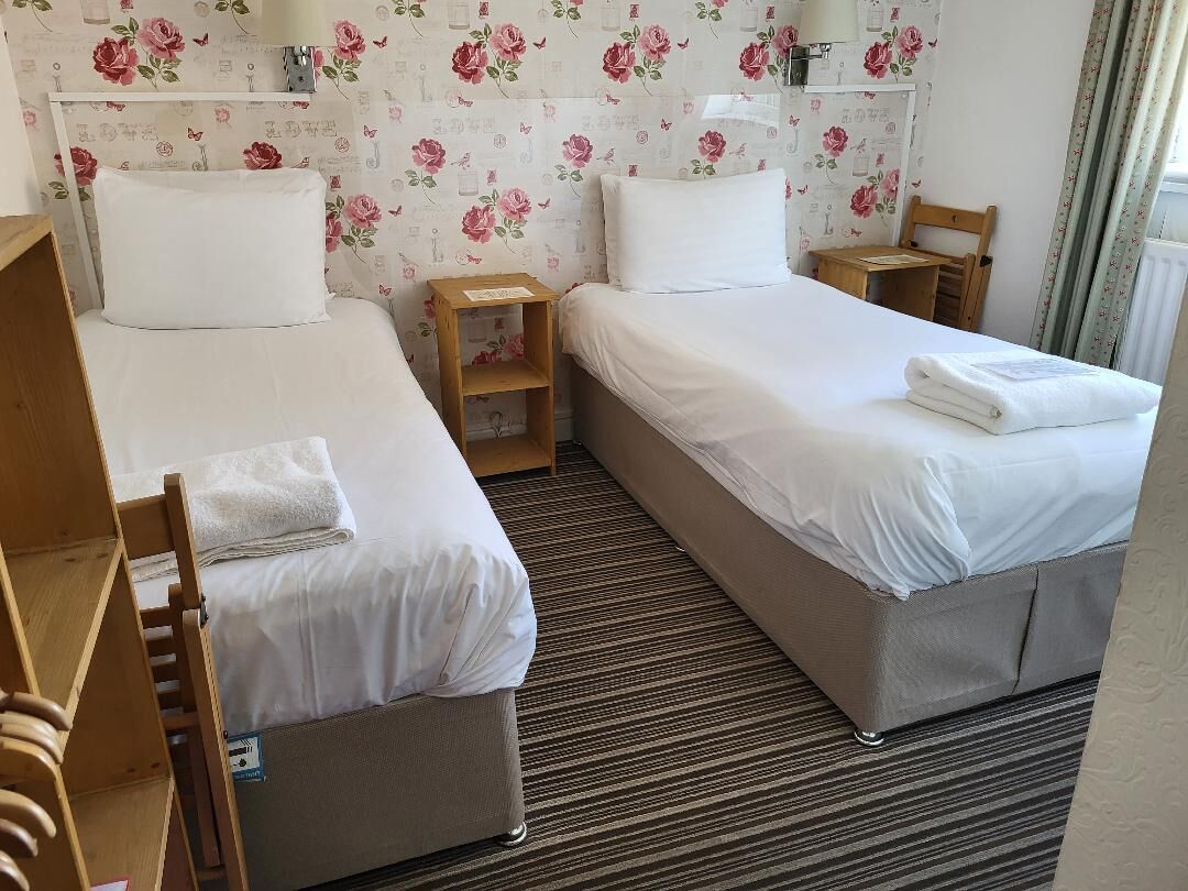 A hotel room with two beds, wooden headboards, and a floral-patterned wallpaper.