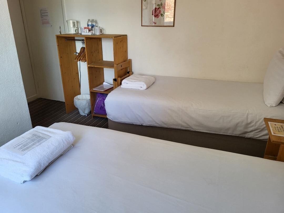 A hotel room with two beds, a wooden shelf with toiletries, and a small table.