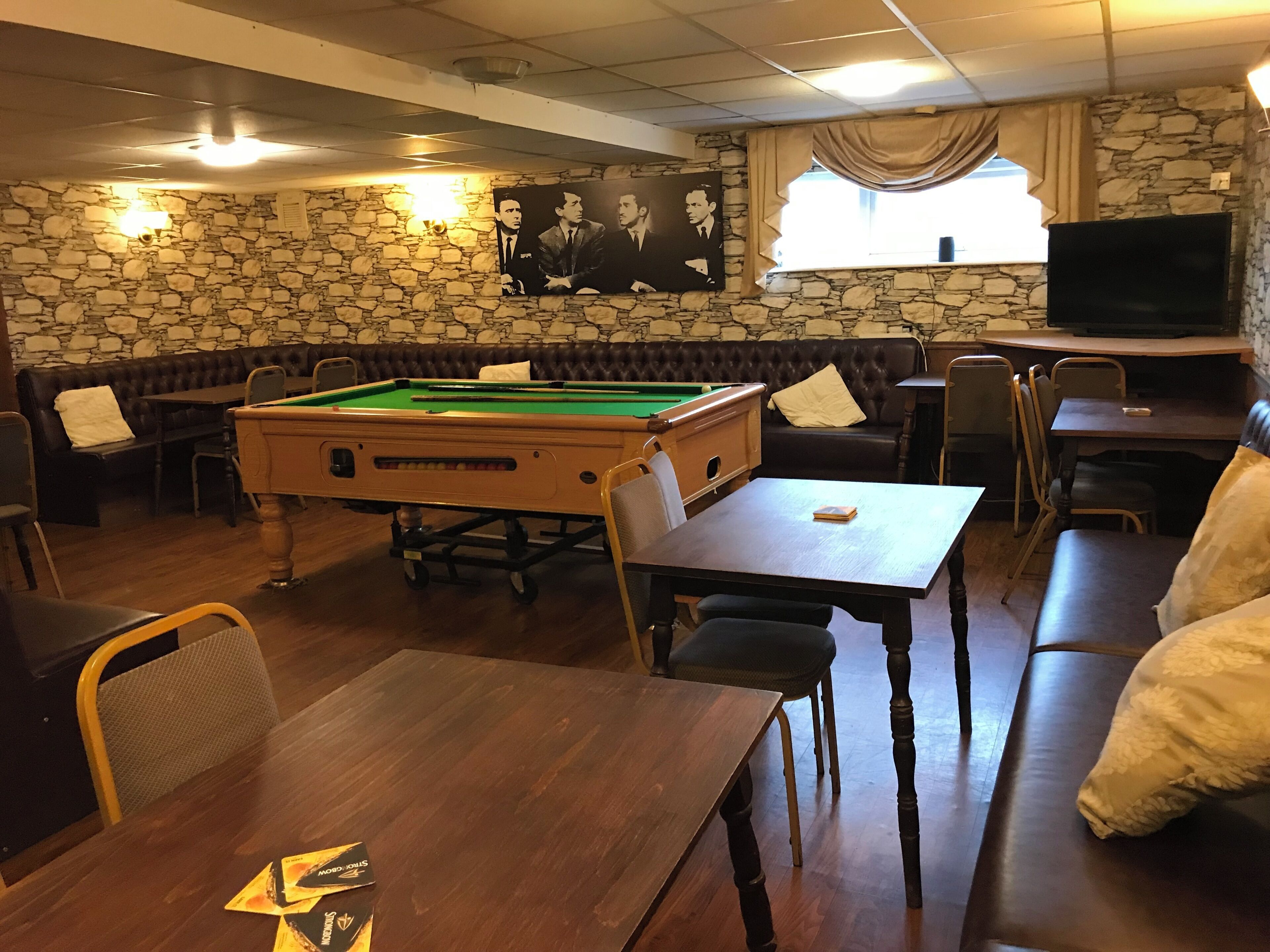 A billiards room with a pool table, seating, and a television.