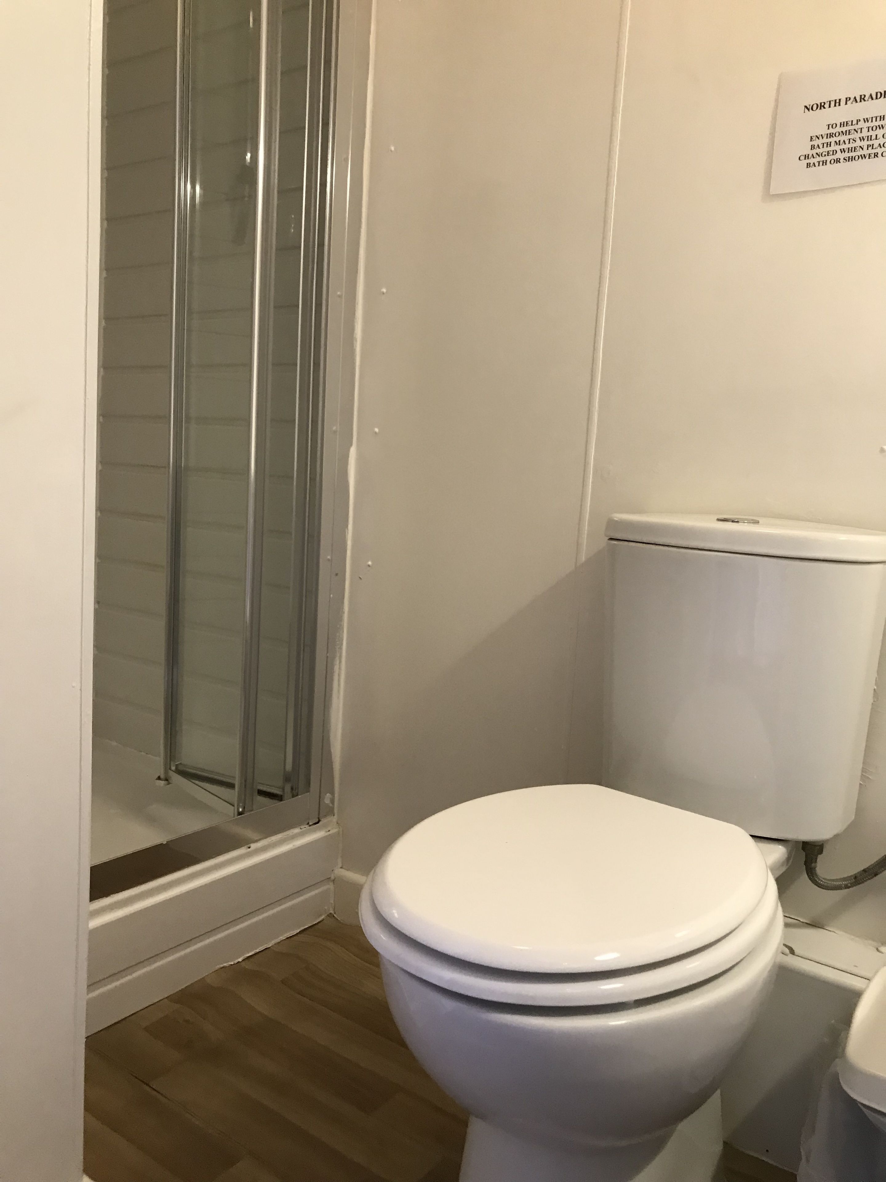 A bathroom with a toilet, a glass shower enclosure, and a white wall with a sign.