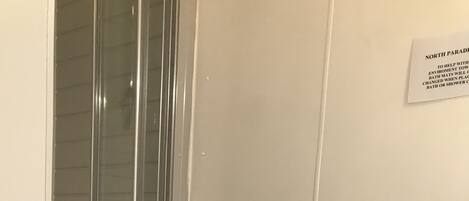 A bathroom with a toilet, a glass shower enclosure, and a white wall with a sign.