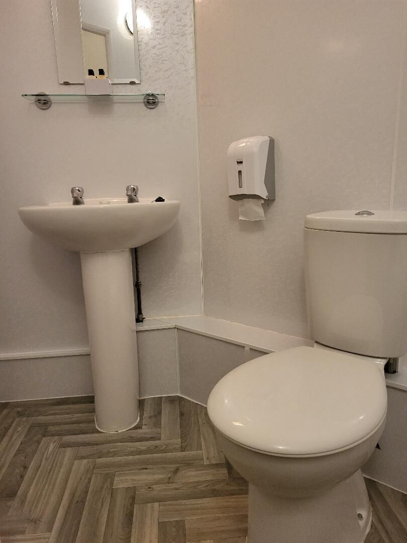 A bathroom with a white sink, toilet, and a soap dispenser on the wall.