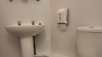 A bathroom with a white sink, toilet, and a soap dispenser on the wall.