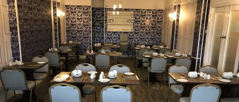 A restaurant with multiple tables and chairs, a patterned wall, and a chandelier.
