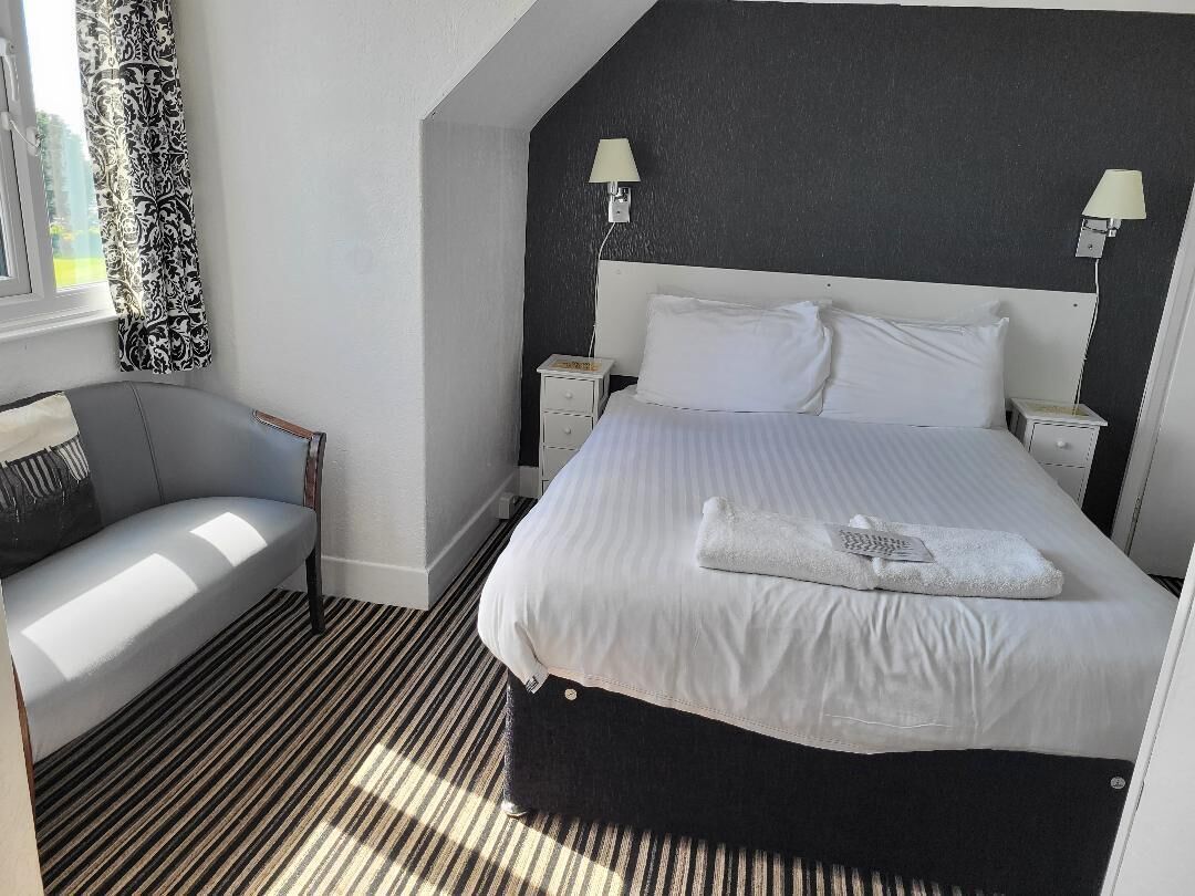 A hotel room with a bed, bedside tables, a chair, and a window with curtains.