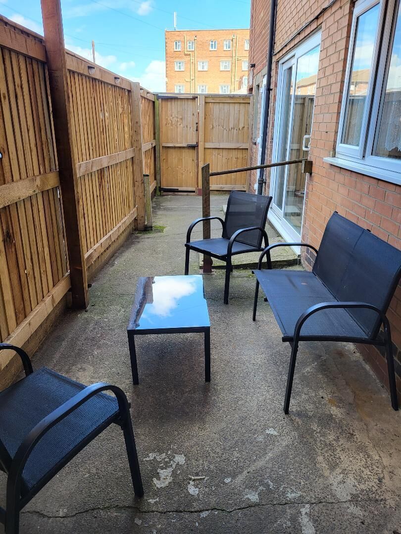 A patio with a wooden fence, a table, and two chairs.