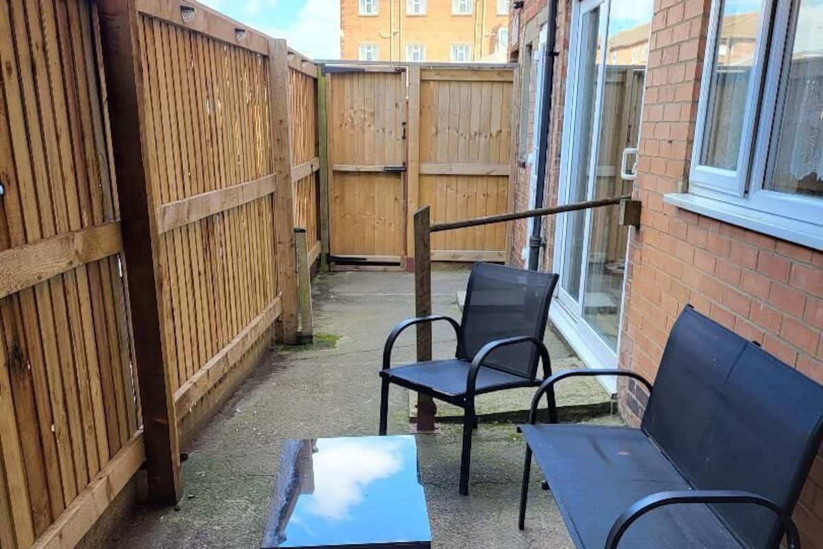 A patio with a wooden fence, a table, and two chairs.