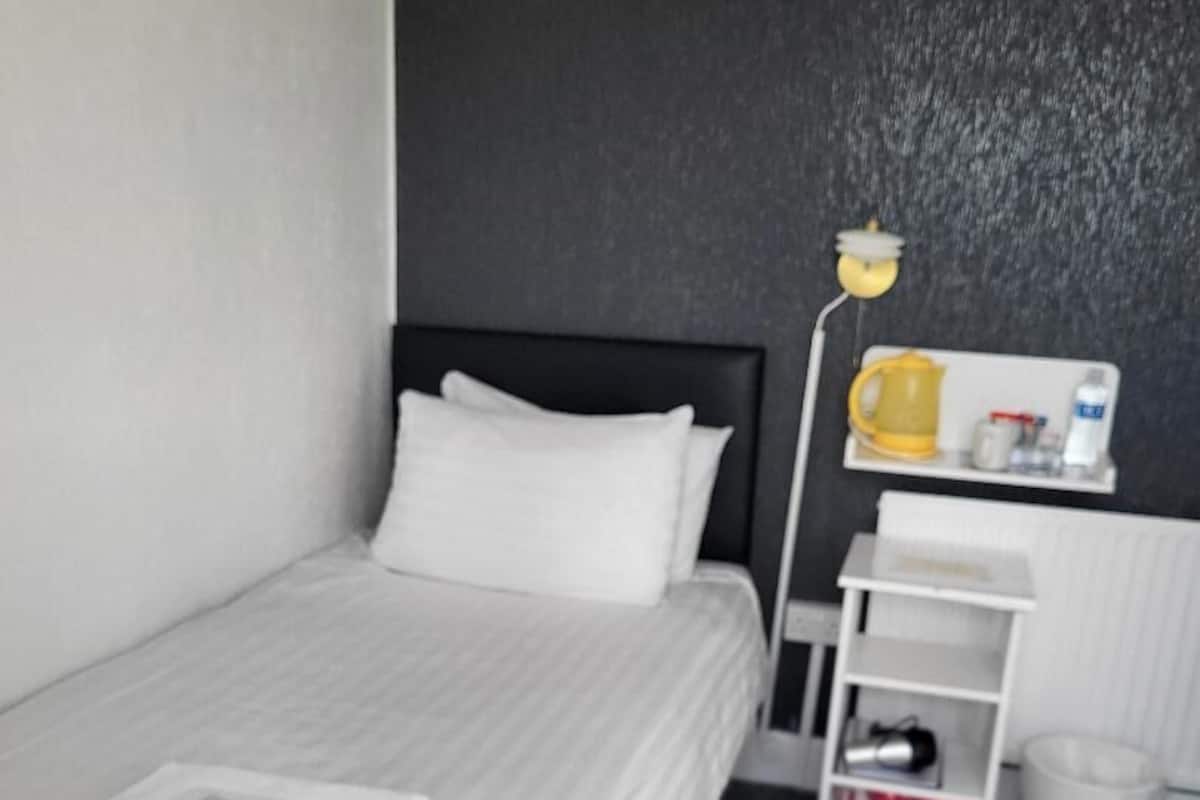A hotel room with a bed, a nightstand, a lamp, a shelf with toiletries, and a radiator.