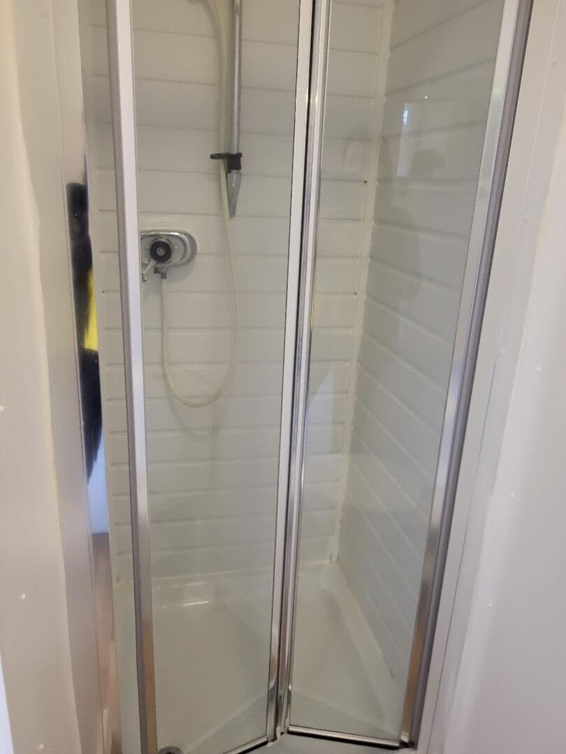 Une cabine de douche fermée par des parois en verre, dotée d’un pommeau de douche à main et d’un robinet de contrôle fixé au mur.
