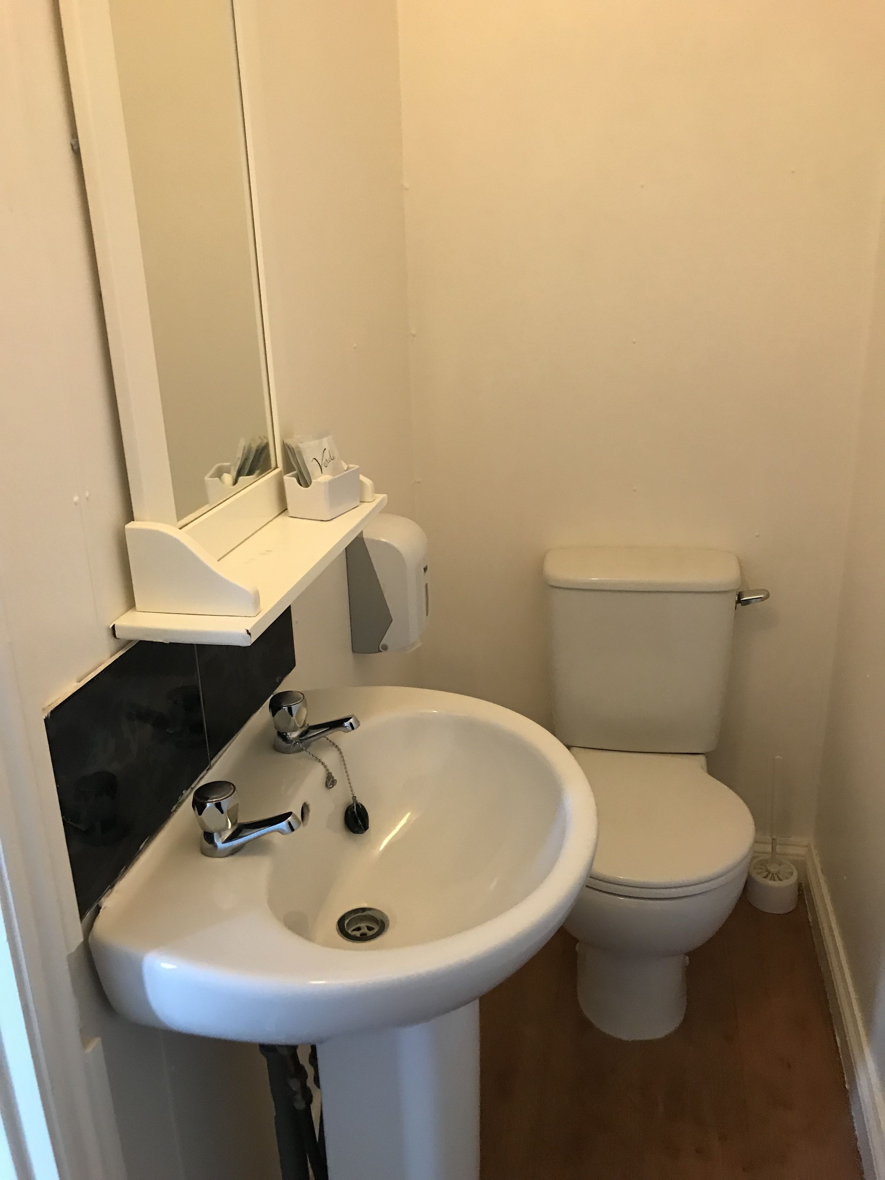 Un bagno con un lavandino bianco, uno specchio, un water e una scatola di fazzoletti a parete.