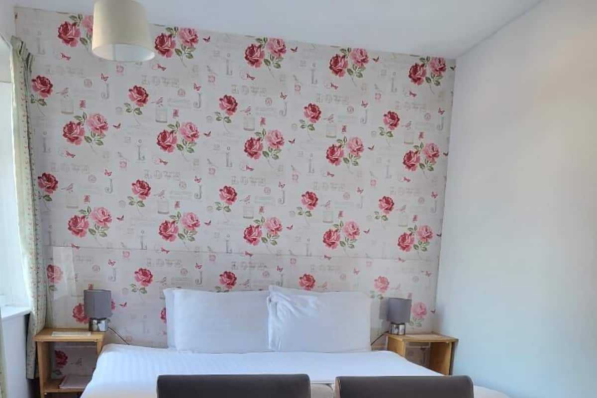 A hotel room with a bed, two armchairs, a nightstand, a lamp, and a floral wallpaper.