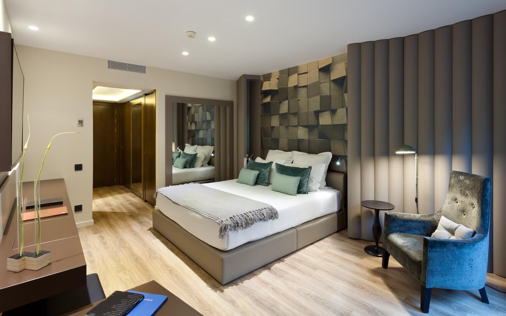 A modern bedroom with a large bed, a desk with a laptop, a chair, and a mirror.