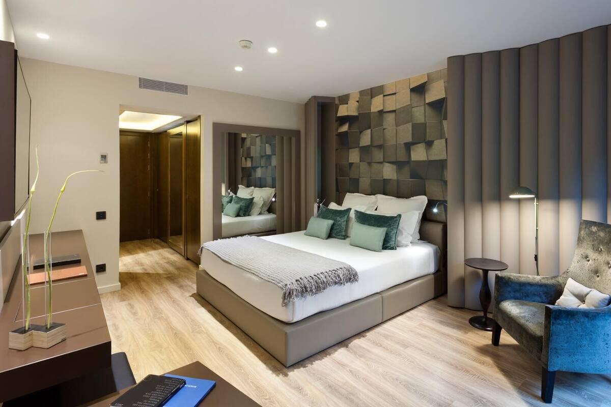 A modern bedroom with a large bed, a desk with a laptop, a chair, and a mirror.