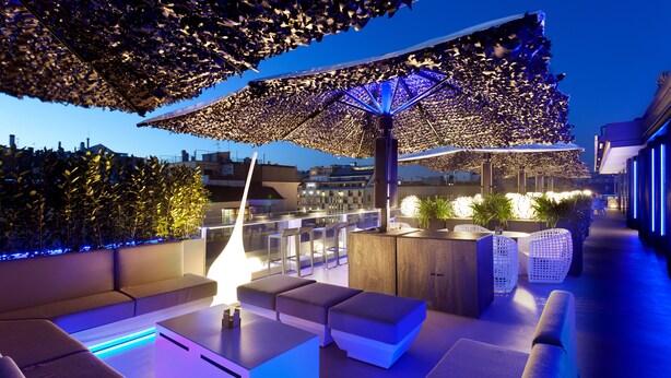 A rooftop lounge with modern seating, a fire feature, and a decorative umbrella.