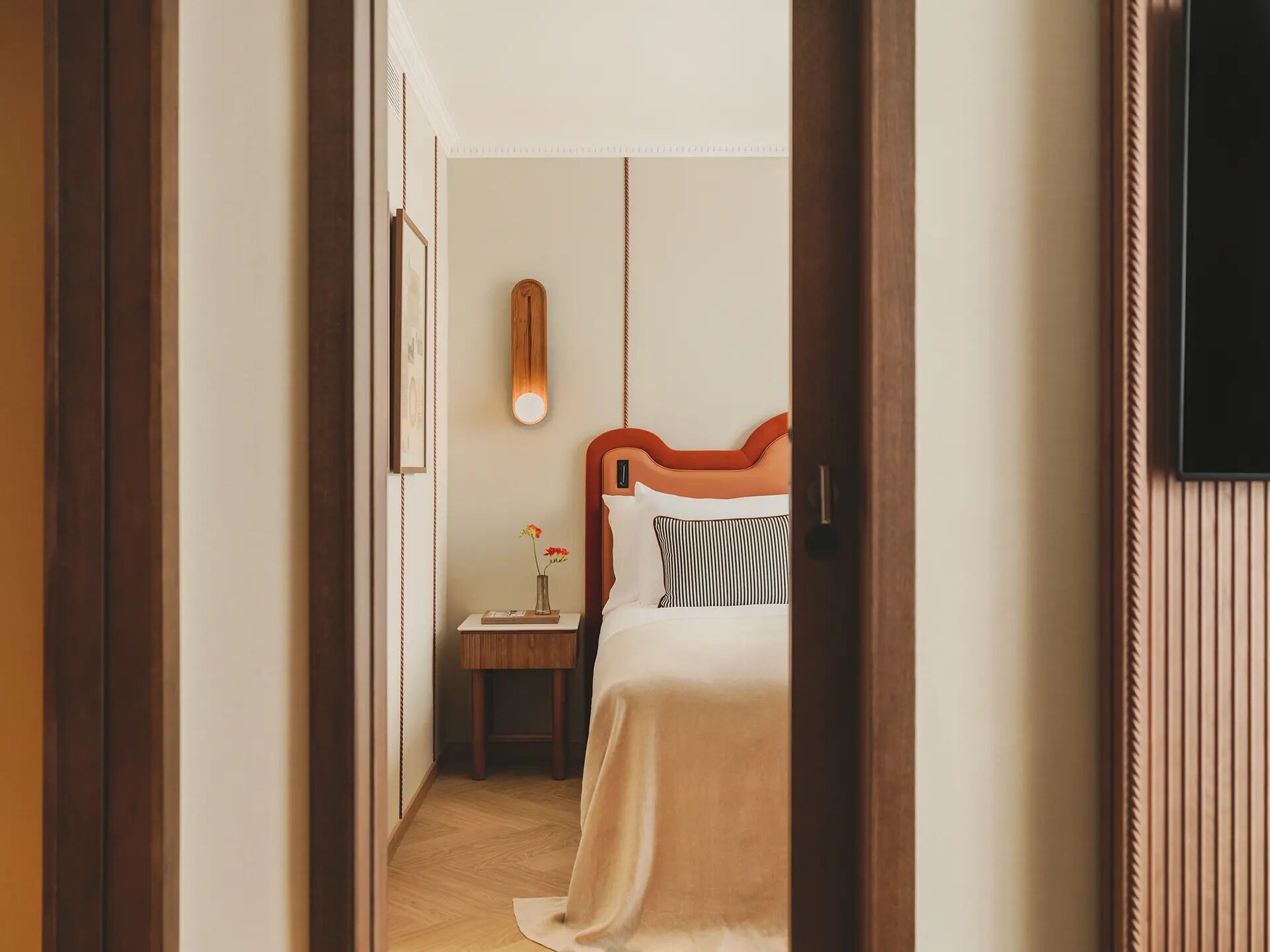 Quarto de hotel com cama, mesa de cabeceira e televisão fixada na parede.