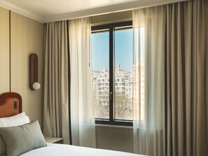 Une chambre d’hôtel avec un lit, une table de chevet, une lampe et une fenêtre avec des rideaux.