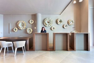 Un interior moderno con un mostrador de recepción de madera, sillas blancas y paneles decorativos en la pared.