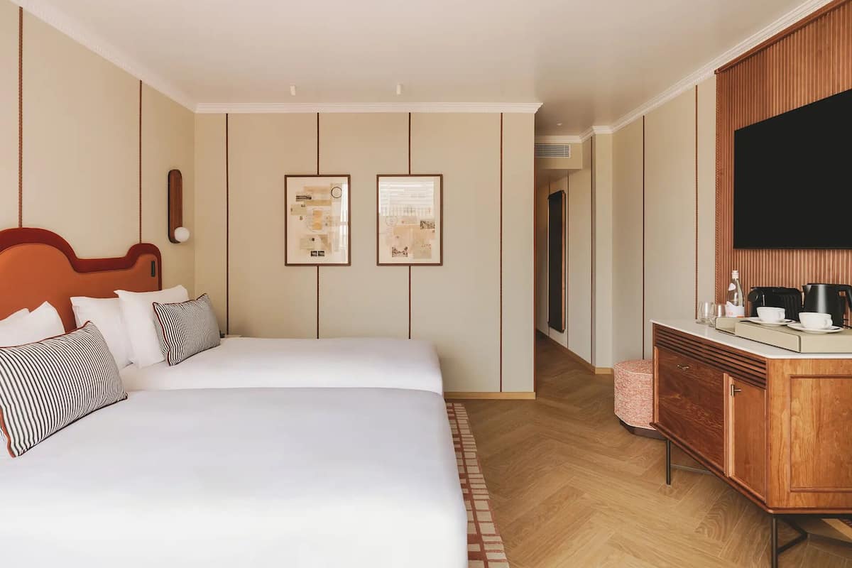Una habitación de hotel con una cama grande, un aparador de madera, un televisor de pantalla plana y dos cuadros en la pared.