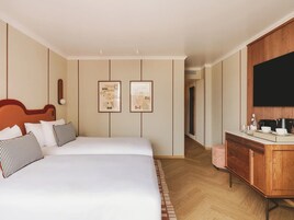 Quarto de hotel com uma cama grande, penteadeira de madeira, TV de tela plana e duas imagens emolduradas na parede.