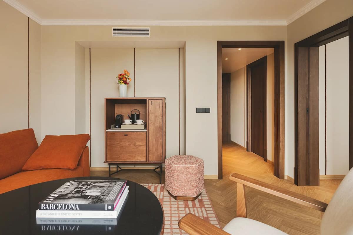 Una sala de estar moderna con un sofá, una mesa de centro con libros, un armario de madera con un jarrón y un pasillo que conduce a otra habitación.