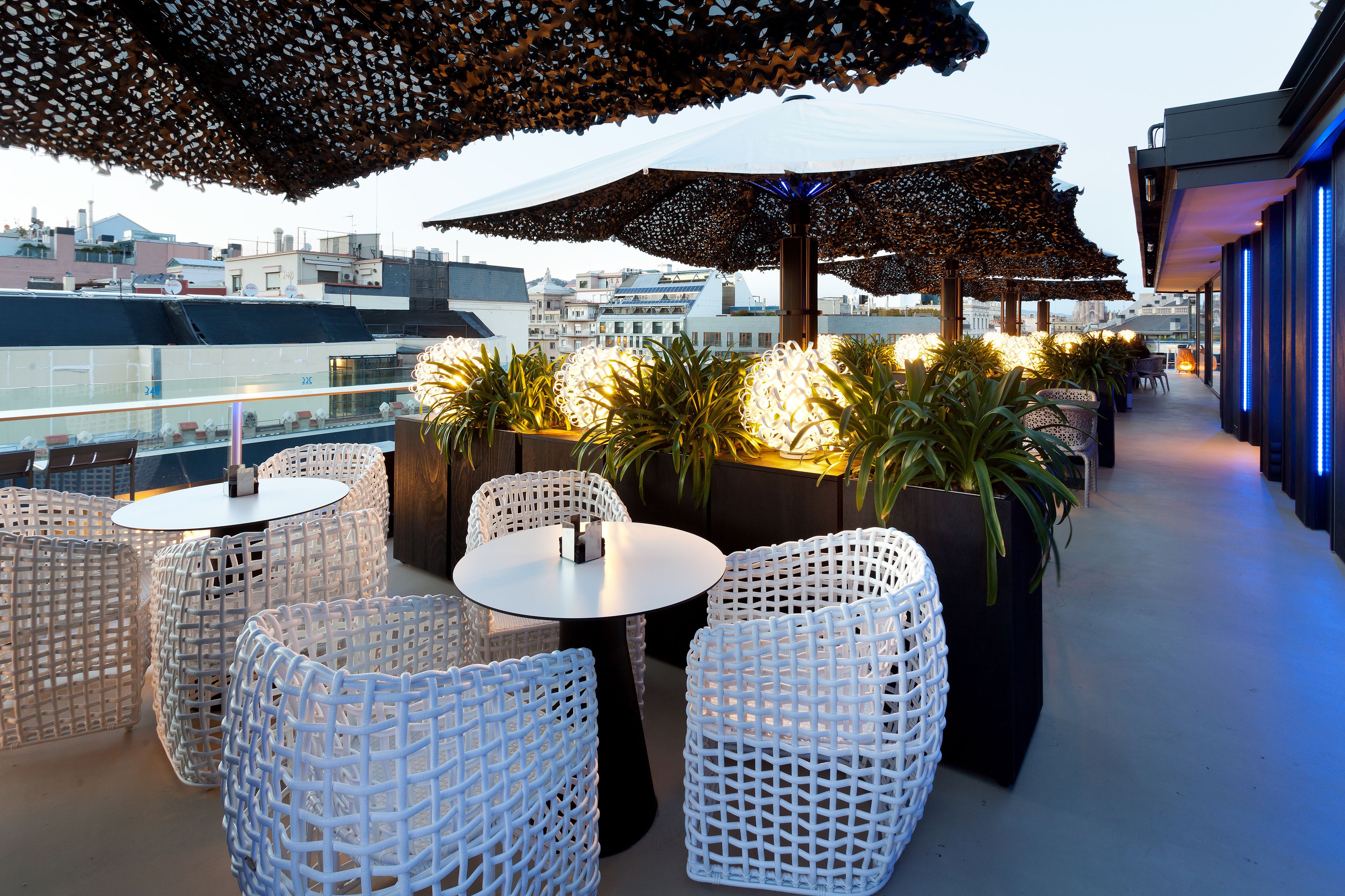 Terraza en la azotea con muebles de mimbre blanco, sombrillas y plantas en macetas.