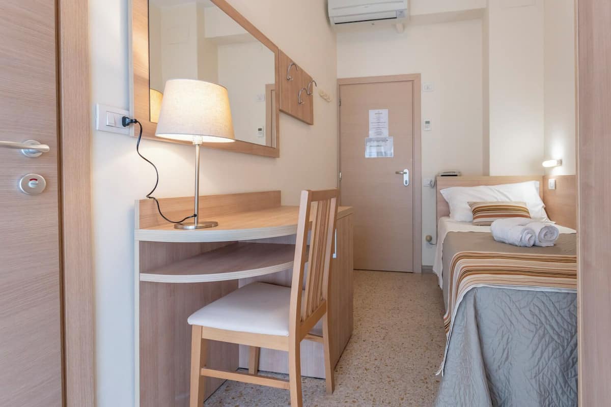 Quarto de hotel compacto com escrivaninha, cadeira e cama.