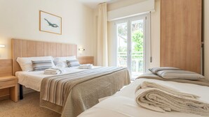 Ett hotellrum med två sängar, en sänggavel i trä, en inramad tavla på väggen och utsikt över grönskan utanför fönstret.