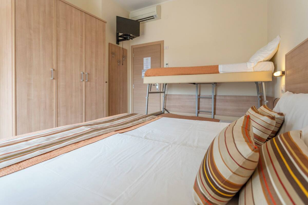 Uma cama de solteiro com encosto, um guarda-roupa de madeira e uma mesinha.