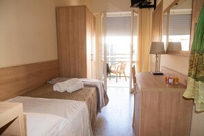A hotel room with two beds, a wooden wardrobe, a desk with a lamp, and a balcony with chairs. - Hotel Cormoran (Riccione)