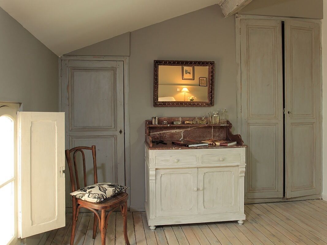 Una habitación con un armario blanco, una silla con cojín floral, un espejo con marco de fotos y una puerta cerrada.