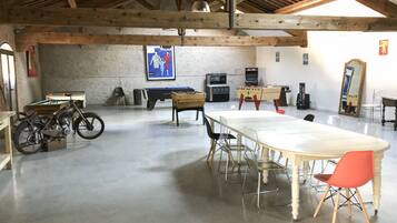 Una habitación amplia con una mesa larga, sillas, una motocicleta, mesa de billar y mesa de fútbolín.