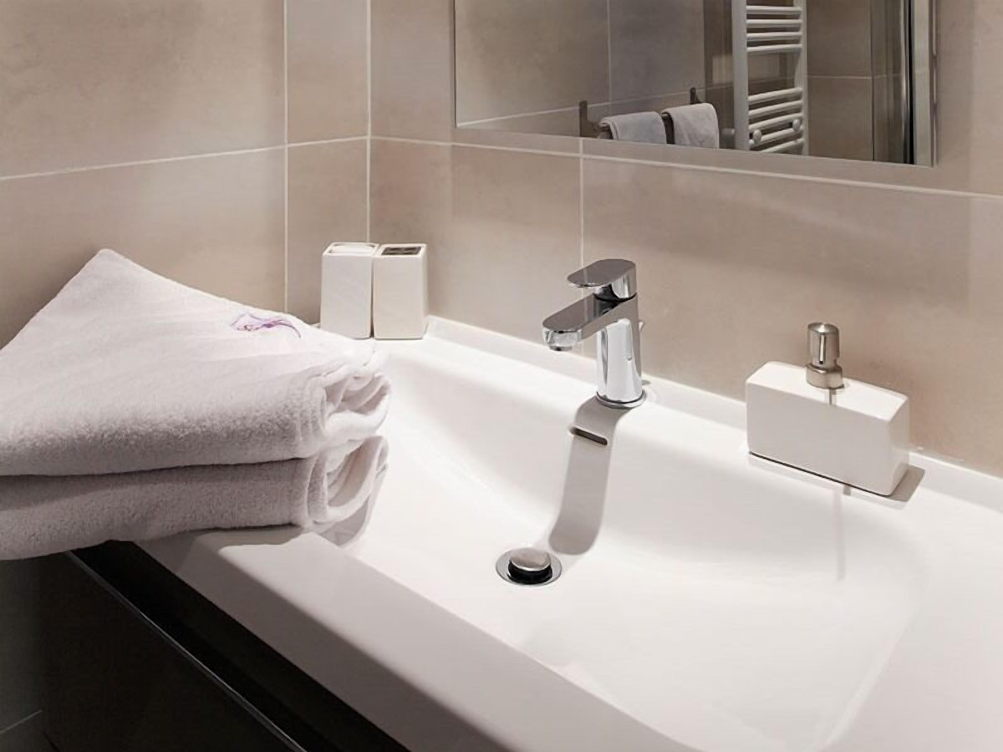 A modern bathroom with a white sink, chrome faucet, and a towel rack.
