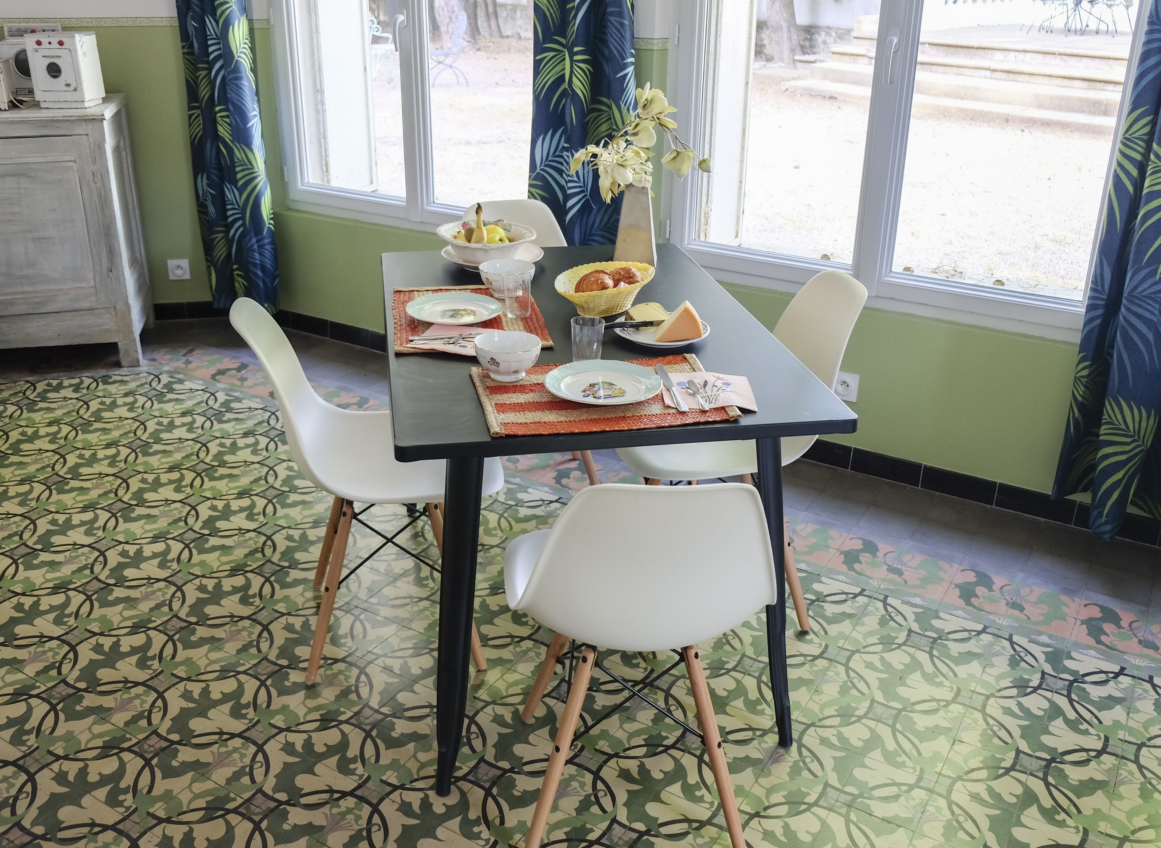 Een eethoek met een tafel voor vier personen, stoelen, een vaas met bloemen en een raam met gordijnen.