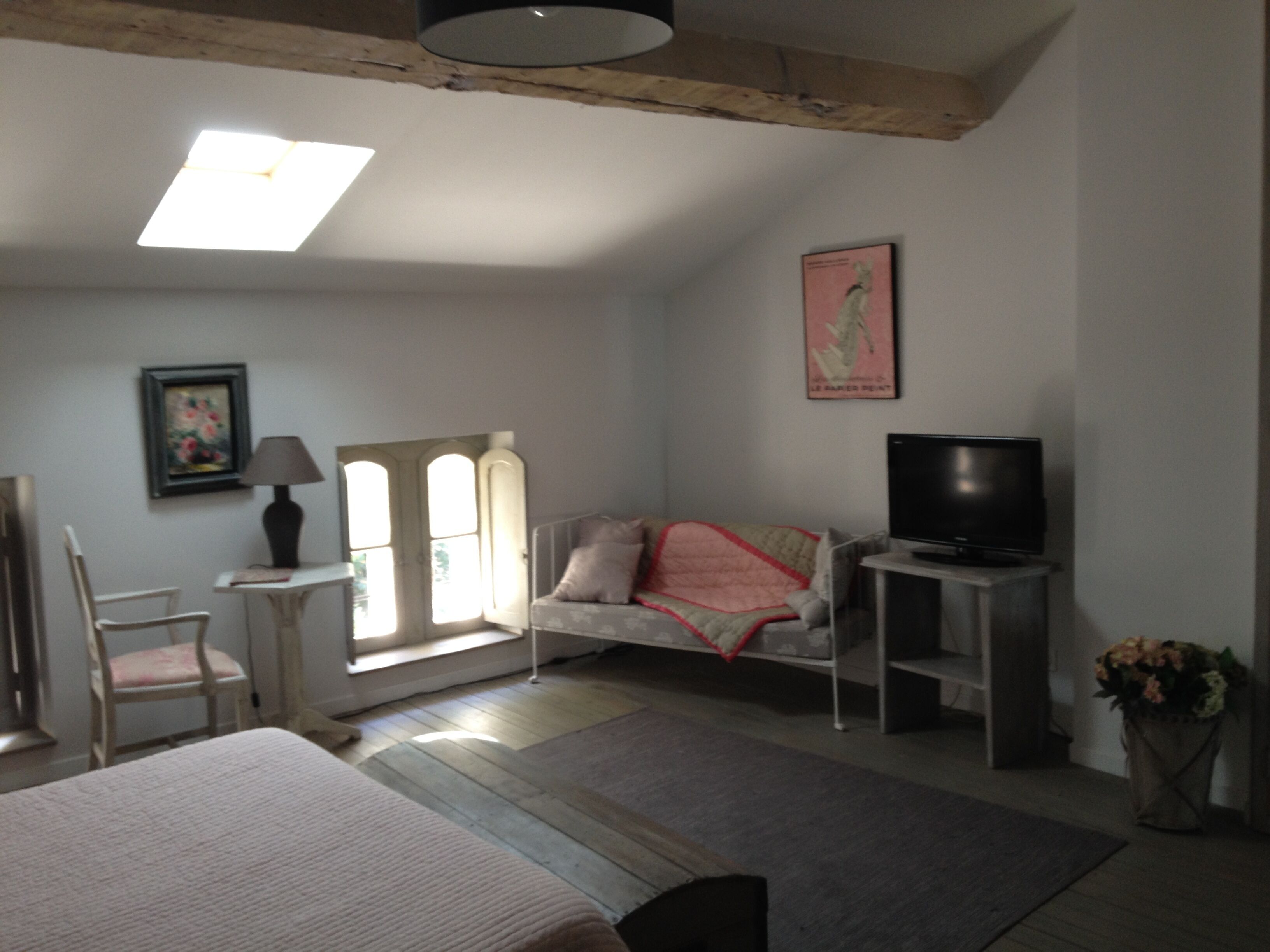 A bedroom with a bed, a chair, a television, a lamp, a window, and a painting on the wall.