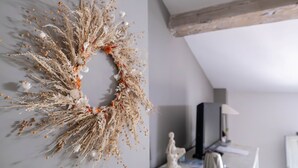 A room with a decorative wreath on the wall, a desk with a lamp, and a television.
