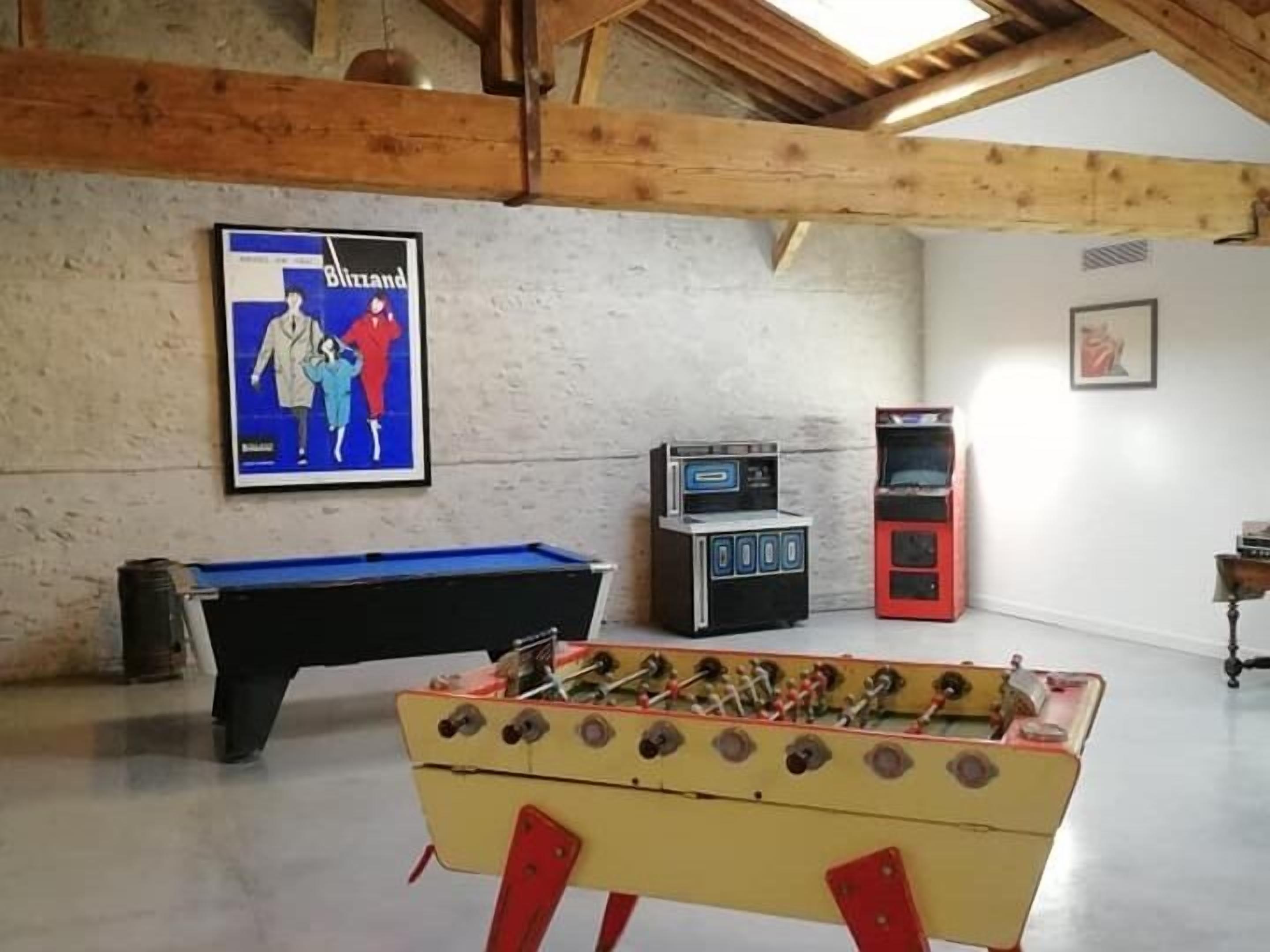 A room with a foosball table, a pool table, and two vintage arcade machines.
