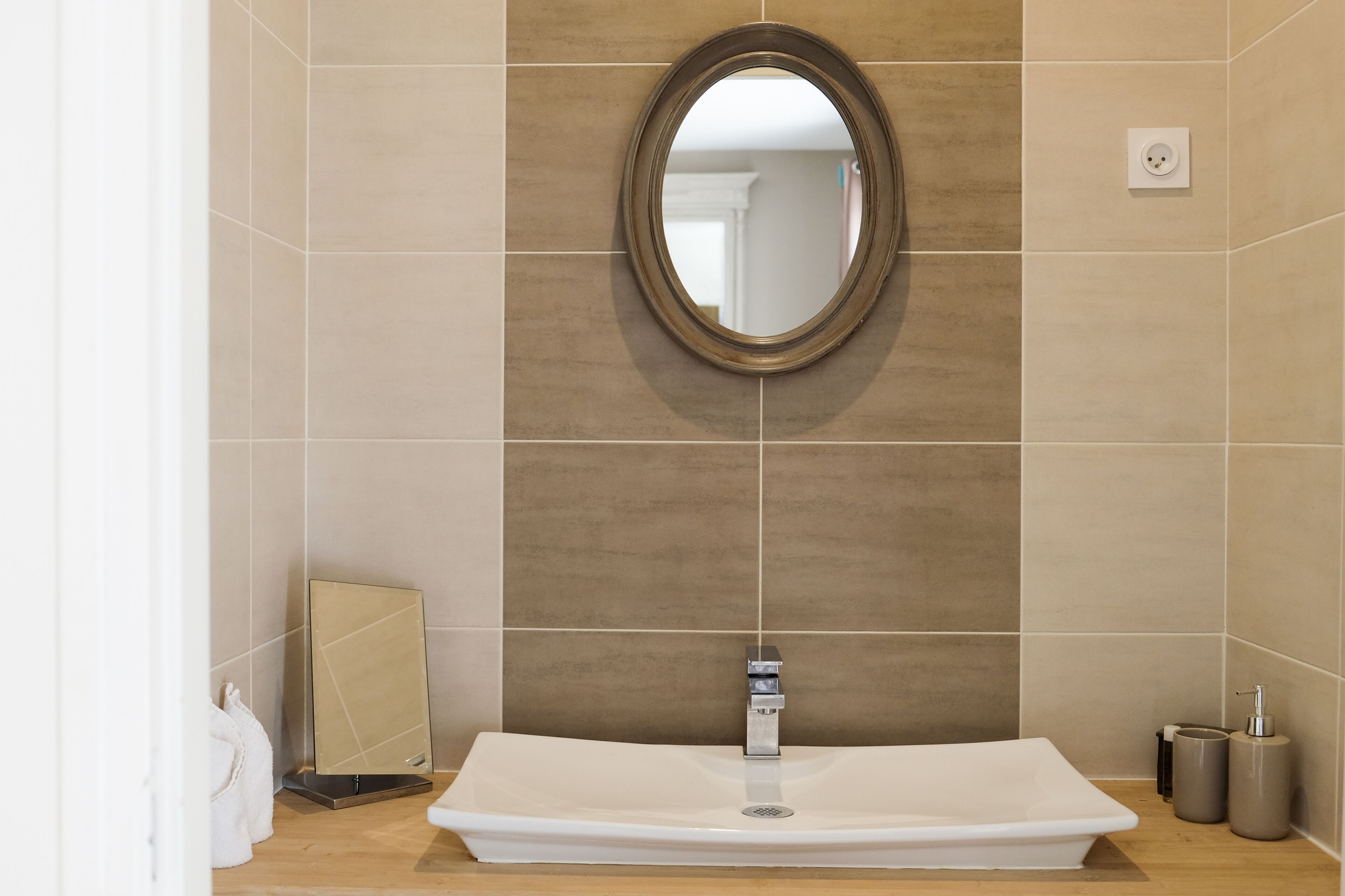 Une salle de bain avec un grand miroir ovale, un lavabo rectangulaire et un porte-serviettes.