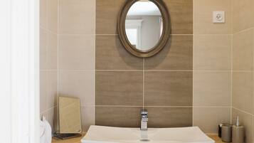 Une salle de bain avec un grand miroir ovale, un lavabo rectangulaire et un porte-serviettes.