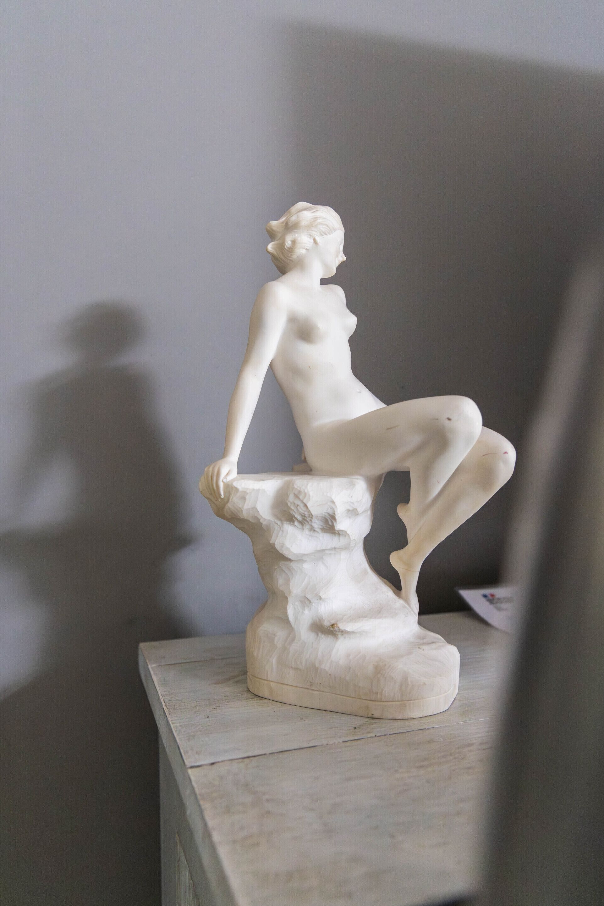 Una estatua de mármol blanco que representa una figura sentada sobre un pedestal.