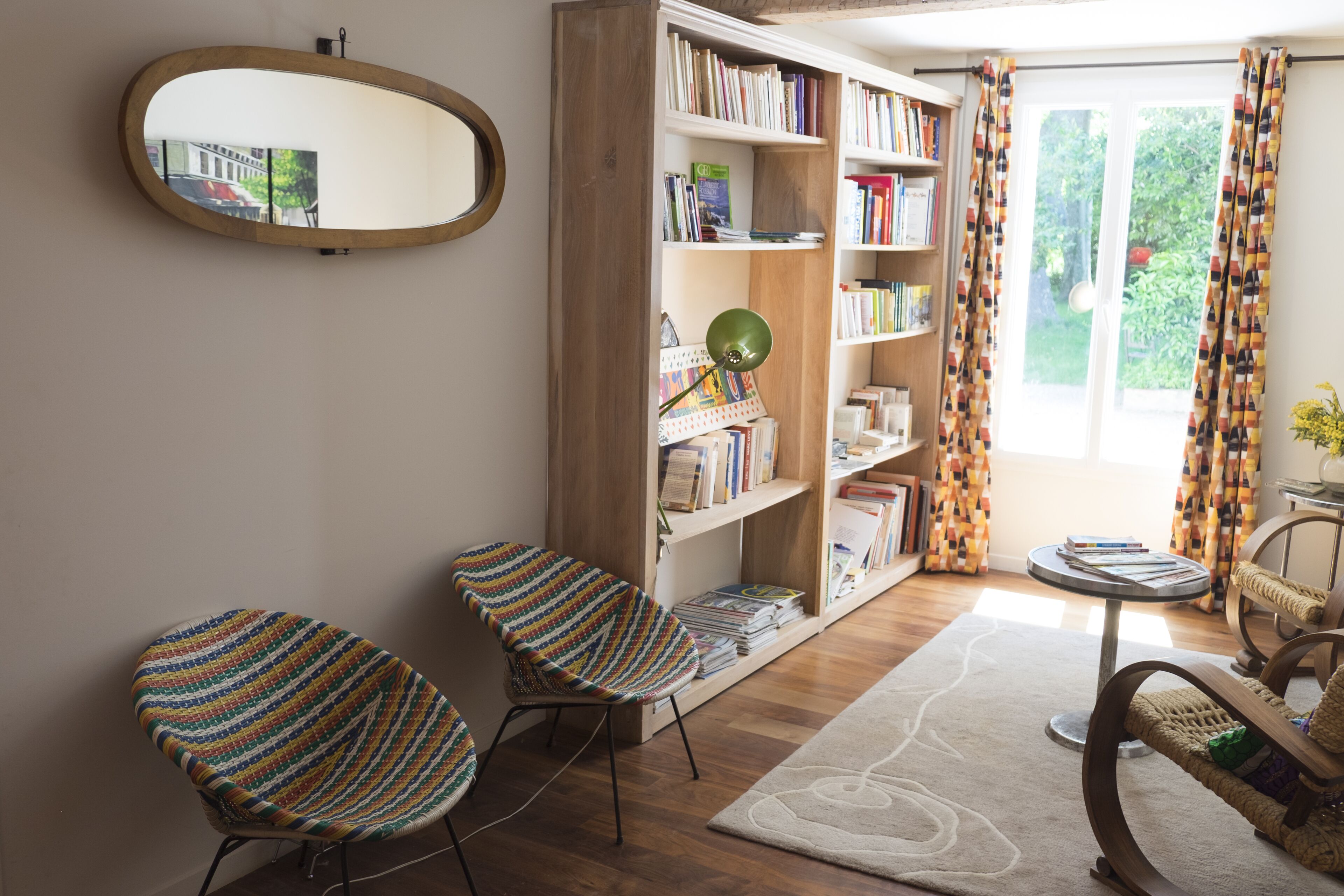 Een leeshoek met twee gestreepte stoelen, een boekenkast, een spiegel en een raam met gordijnen.
