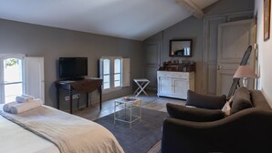A spacious bedroom with a large bed, a wooden desk, a television, and a cozy seating area.