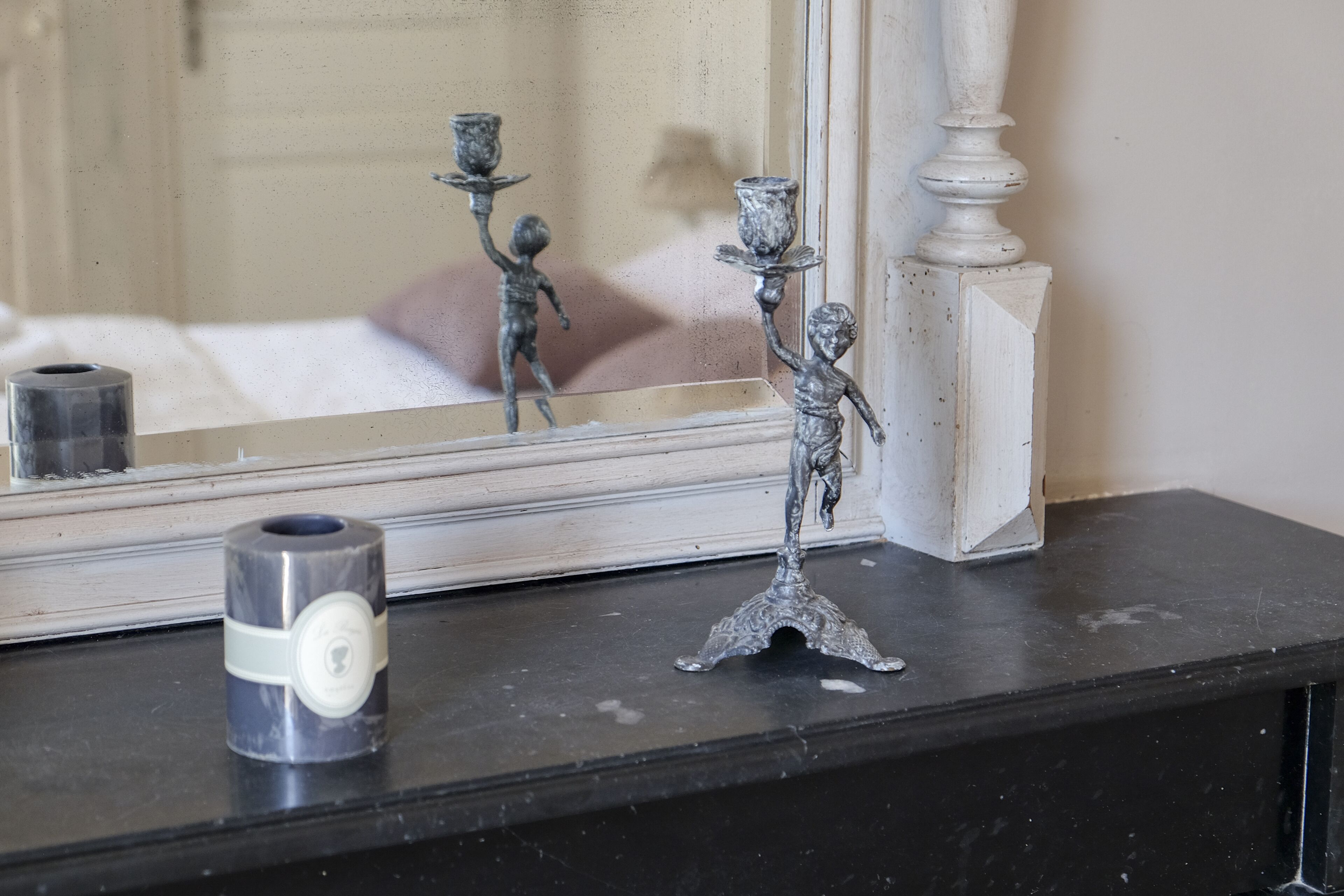 Een spiegel met een decoratieve metalen lijst, een klein metalen kaarsenhouder en een kaars op een zwart oppervlak.