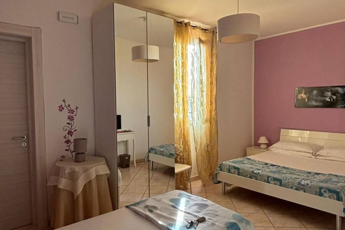 Un dormitorio con dos camas, un espejo, una mesita de noche, una lámpara y una ventana con cortinas.