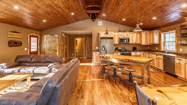 A spacious living area with a wooden ceiling, a kitchen with wooden cabinets, and a bar area with stools. - The Beautiful Whitetail Ridge-Luxury 5BR Cabin, Just minutes from downtown (Wisconsin Dells)