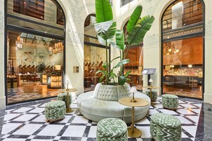 A lobby with a checkered floor, a seating area with a sofa and ottomans, and large windows with decorative elements.