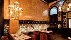Interior de un restaurante con una larga barra, sillas de mimbre y un revestimiento de azulejos decorativos.