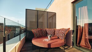Un espacio de descanso al aire libre con asientos redondos, cojines estampados, un cubo metálico y una mesa de vidrio sobre una terraza de madera.