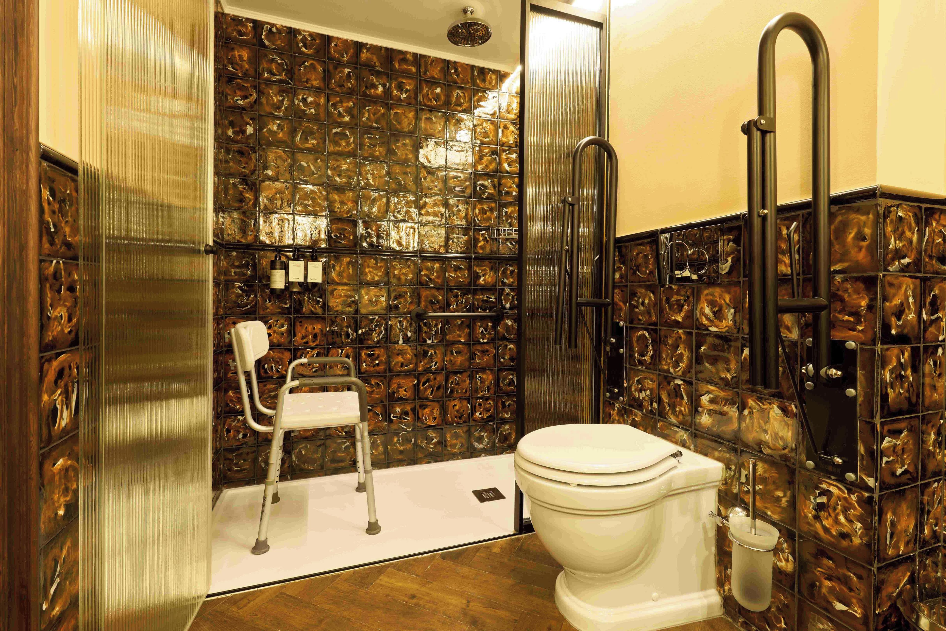 A bathroom with a white toilet, a shower area, and a chair.